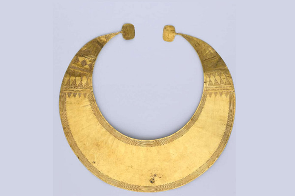 Gold lunula. Flat sheet crescent of beaten gold with quadrangular terminals. It is decorated with a finely-incised and complex geometric pattern. The horns are decorated with horizontal patterns of horizontal lines, concentric triangles, bands of diamond shaped motifs, triangles touching at their apex filled with horizontal lines, rows of small oblique lines